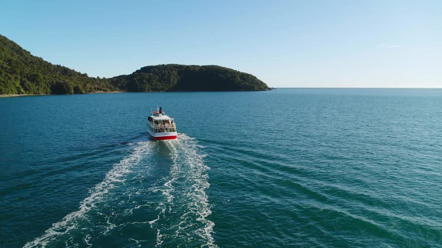 A ferry on the ocean with land the sky and clouds in the background