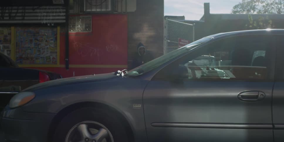 A man stands near a building as a car passes