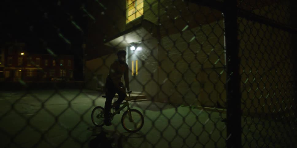 A man is riding a bike behind a fence at night