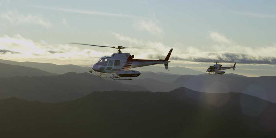 Helicopters fly above a canyon at sunrise