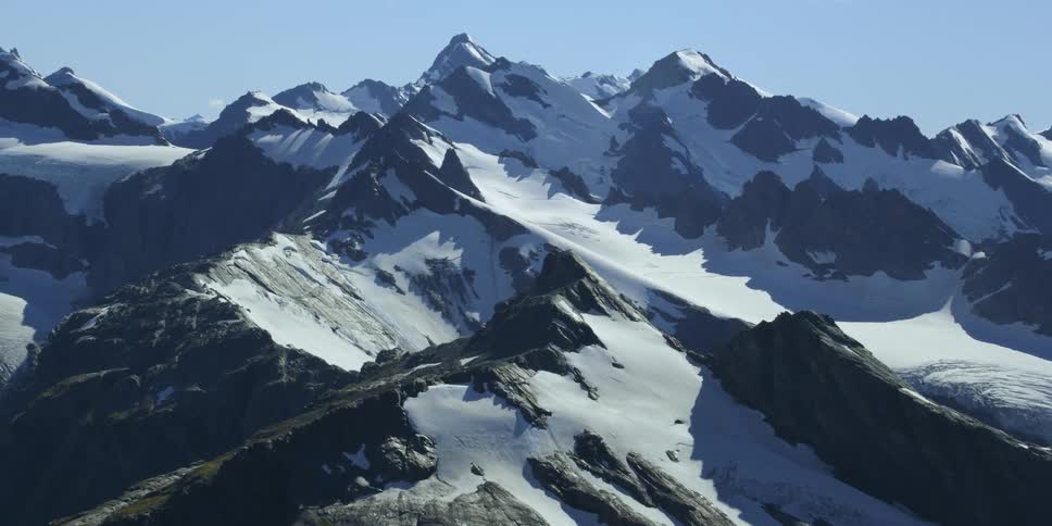 The rocky jagged peaks of a mountain with sun shining down on the snow