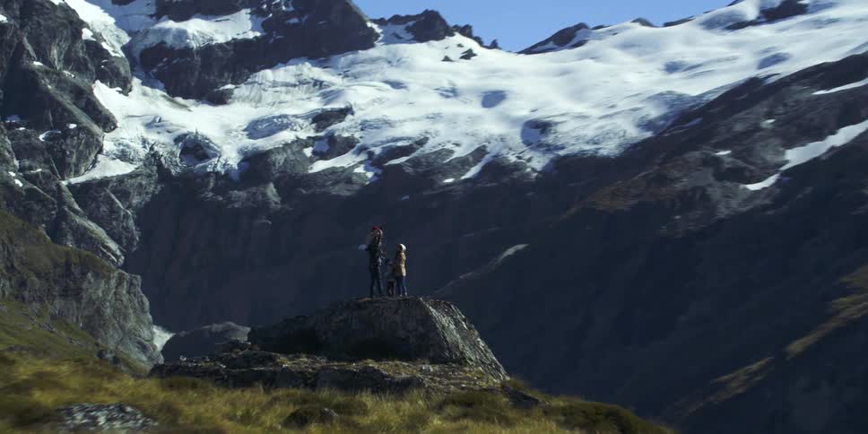 Family stands on a large rock near the snowy mountains