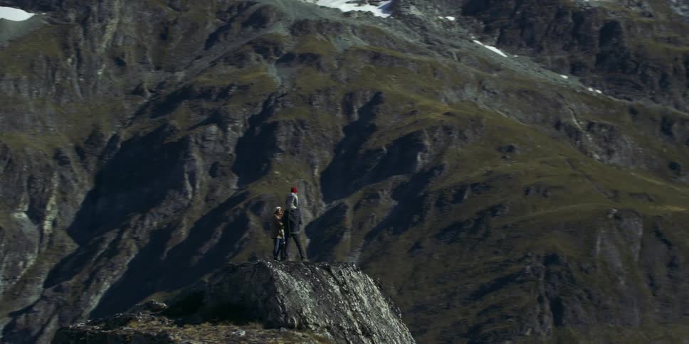 A family stands atop a large mountain cliff looking at the scenery