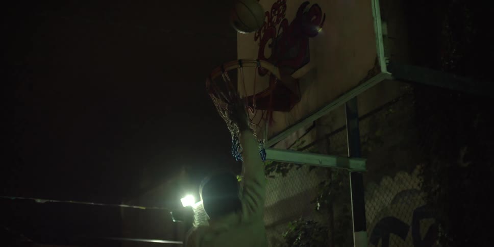 A man takes a basketball shot on an urban basketball court at night