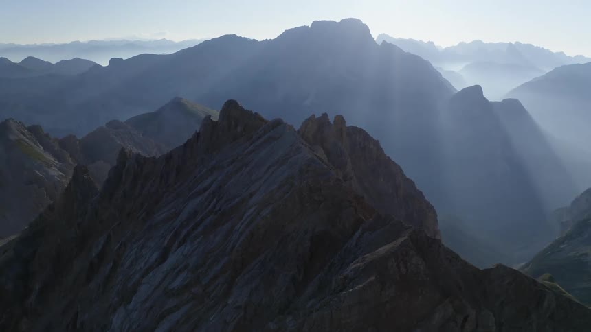 A jagged mountain ridge leading towards a nearby peak shrouded in fog during the day