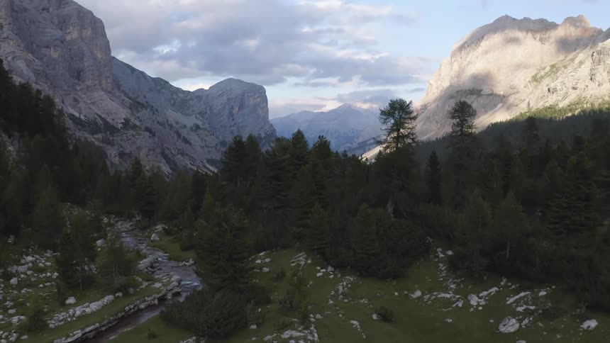 A landscape with a stream trees with a mountain range the sky and clouds in the background