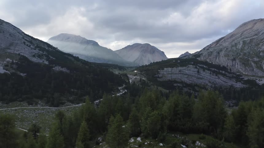 A landscape with hills and trees with a mountain range the sky and clouds in the background