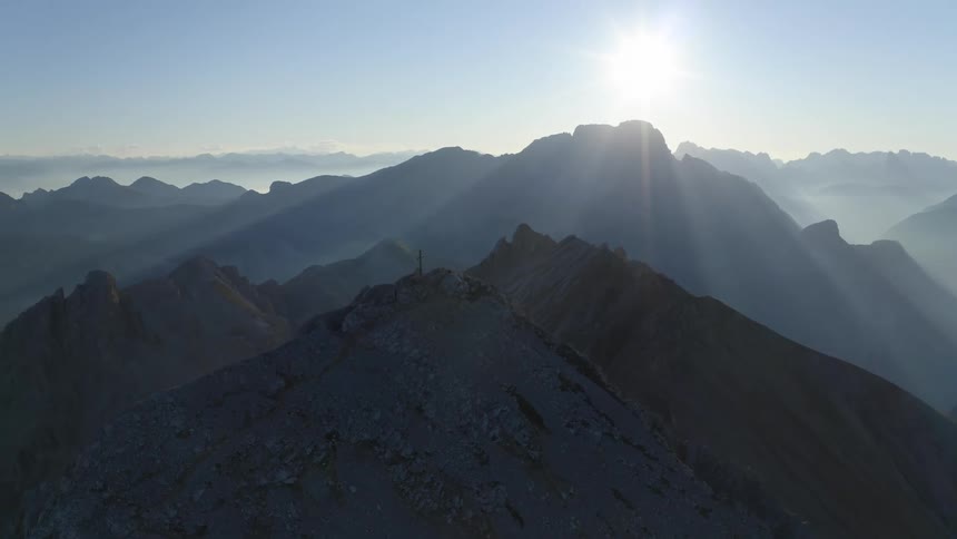 A mountain range with the sun the sky and clouds in the background