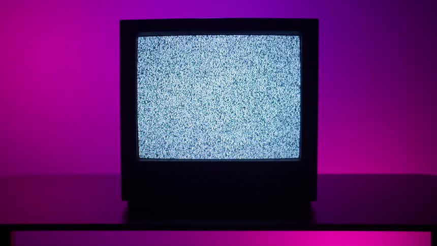 Static flashes on the screen of a retro television that is sitting on a table in front of a pink wall