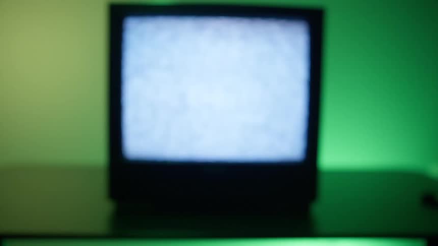 The screen of a small television flickers with static while the lights behind it change colors