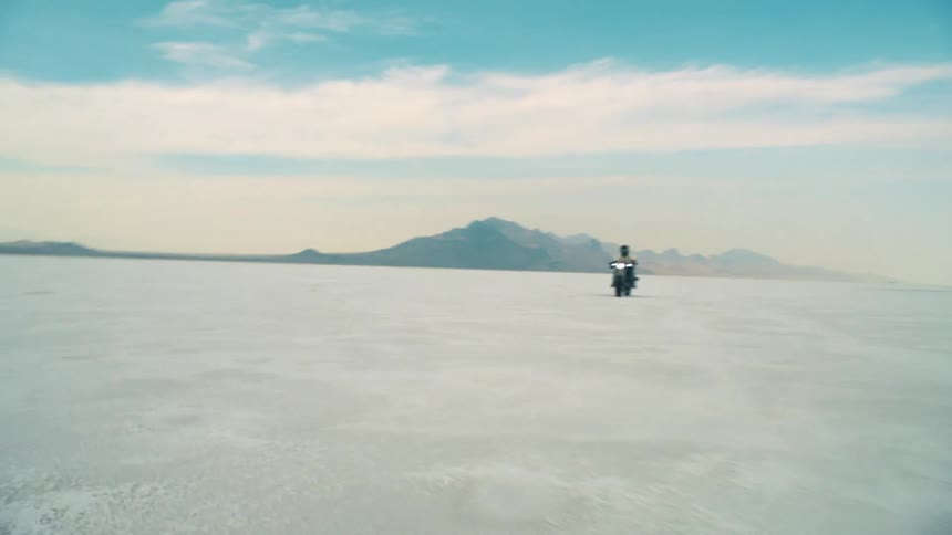 A motorcycle races across empty barren salt flats