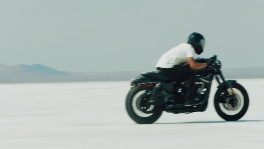 A man is racing his motorcycle across a salt flat while wearing very little protective gear