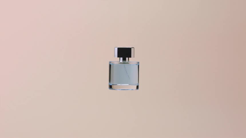 A glass bottle of perfume spins against a colored background