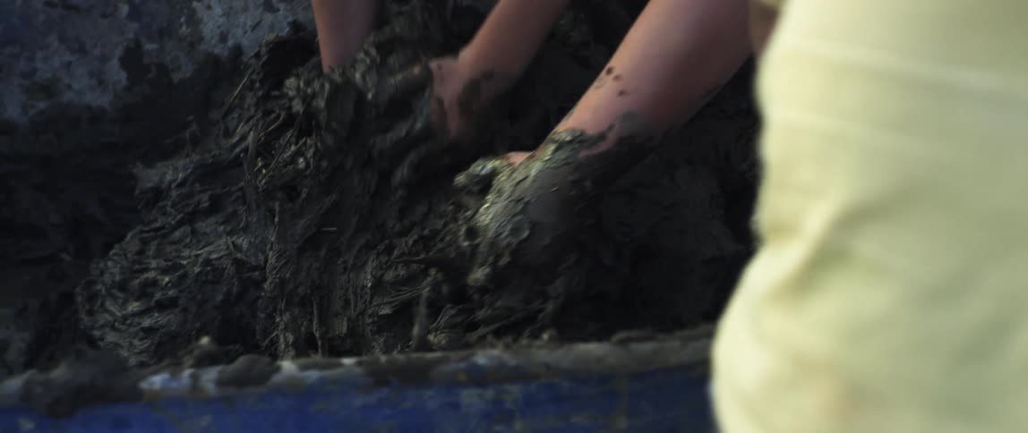 A trio of people scoop up big handfuls of thick and heavy clay