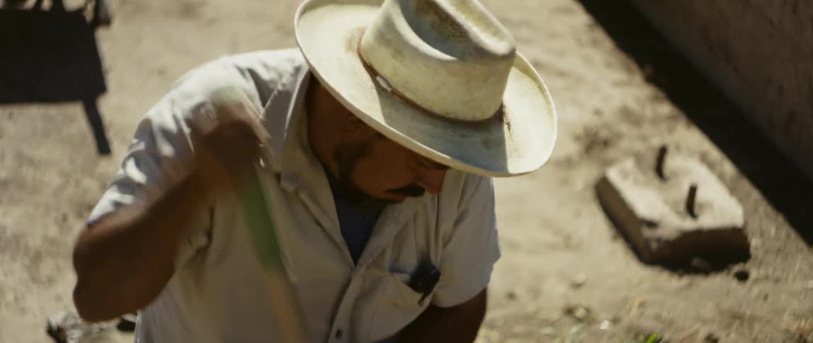 Man wearing sun hat digs large hole in dirt near wall