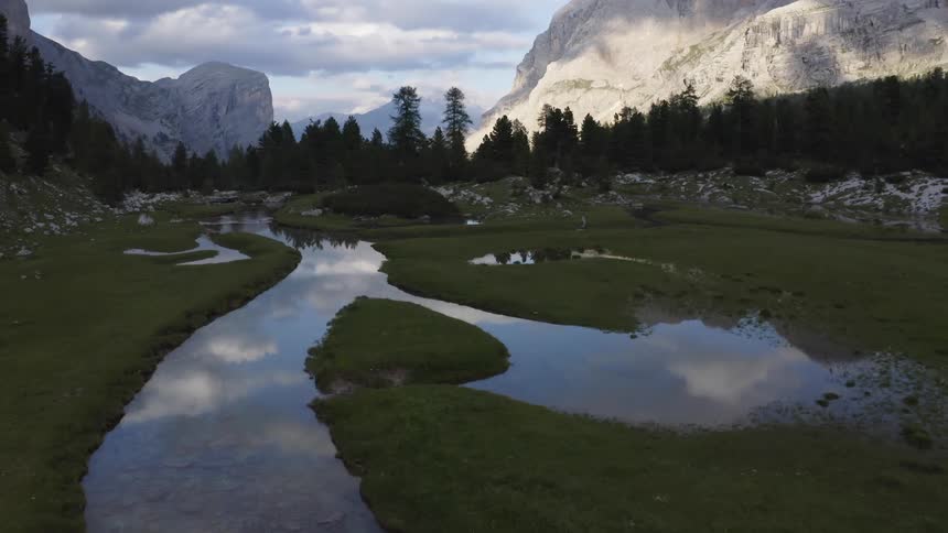 A landscape with a stream trees with a mountain range the sky and clouds in the background