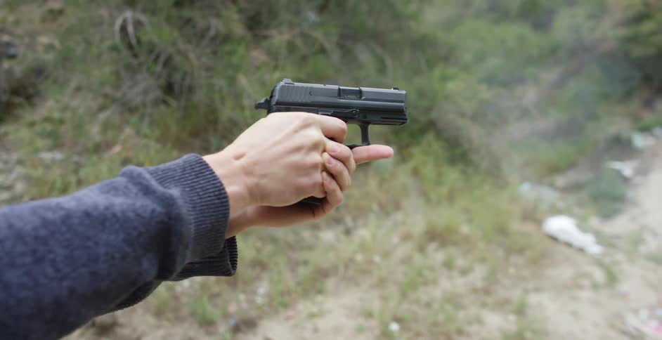 A man fires a handgun next to a hill