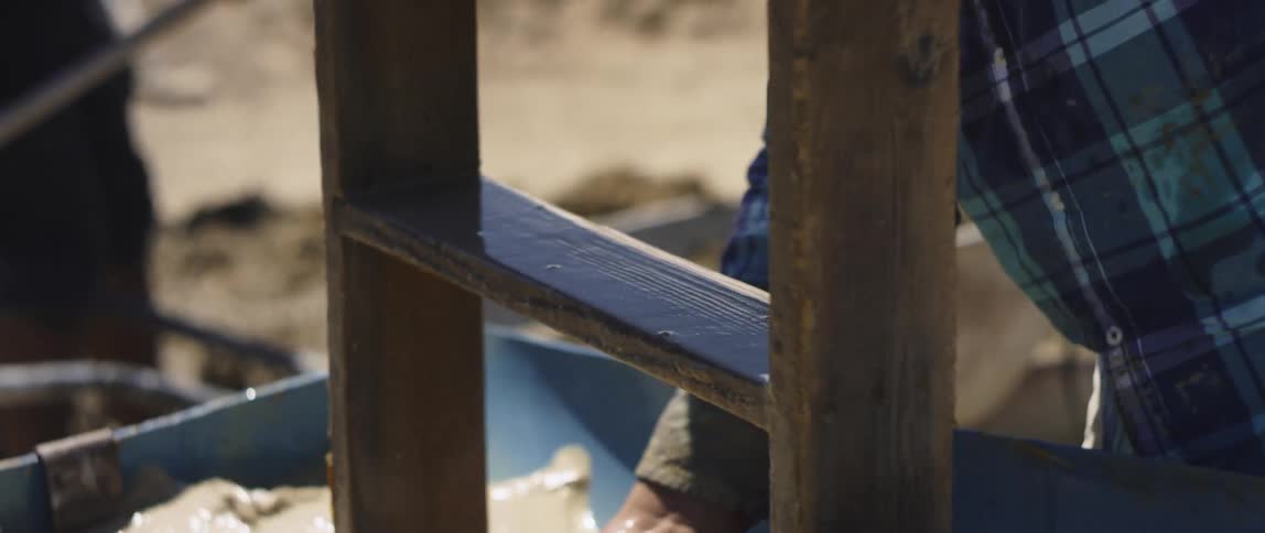 A man washes off a wooden frame in muddy water while a coworker digs a trench
