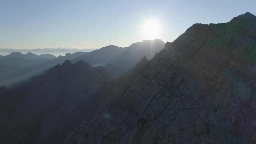 A mountain range with the sun the sky and clouds in the background