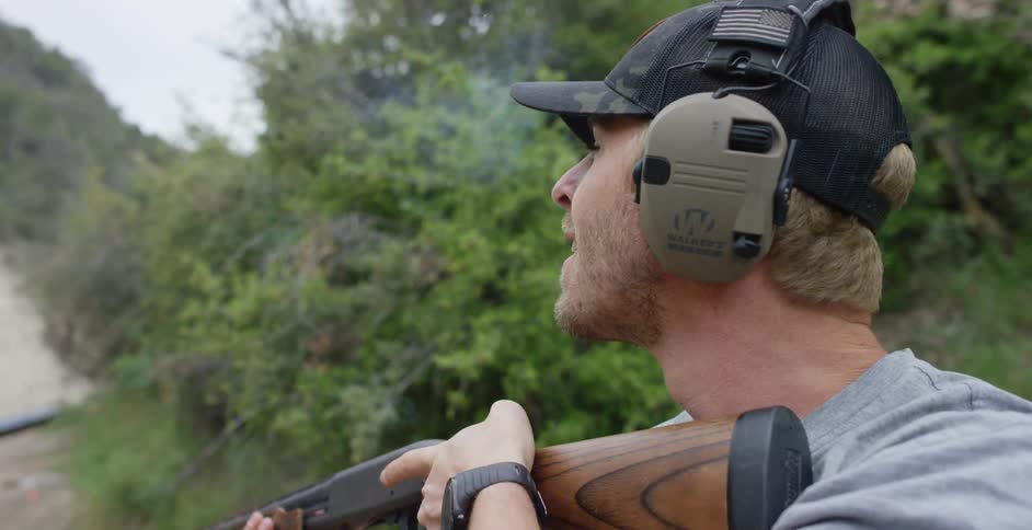 Man wearing ear protection aims and takes shot toward sky before turning with a smile