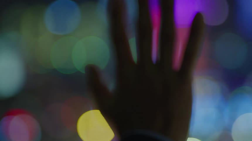 A person holds their hand up in front of bright lights outside at night