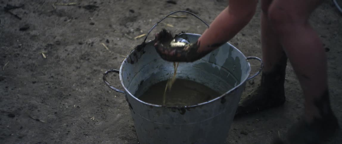 A young girl scoops watery mud out of a metal pail