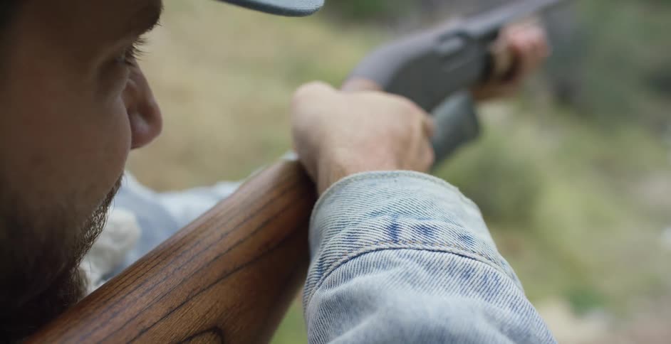 A man shoots a rifle into some nearby vegetation