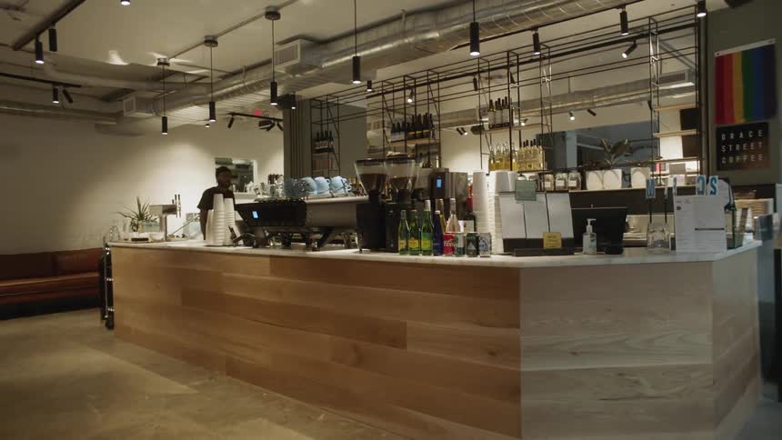 Man walks behind counter holding coffee mugs and coffee beans at coffee shop