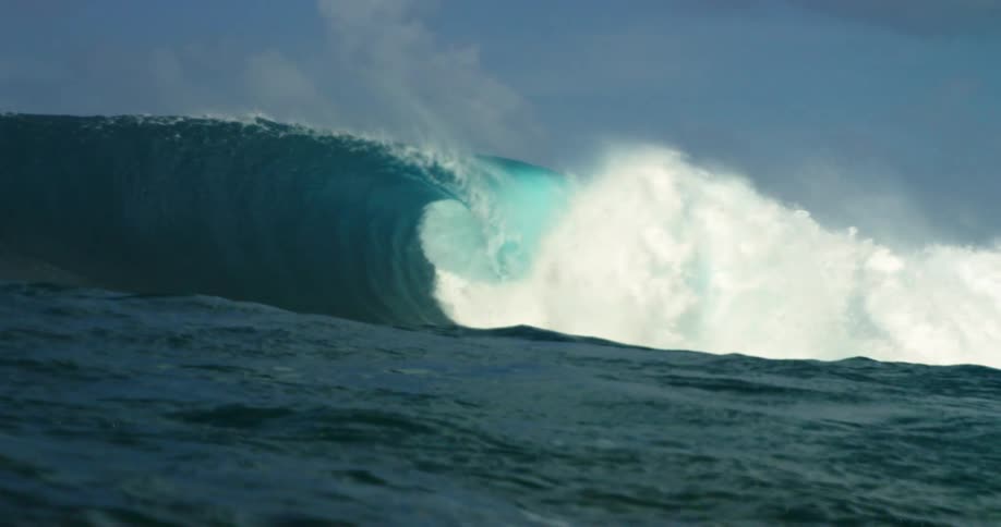 A huge wave rolls in splashing with a few clouds in the sky