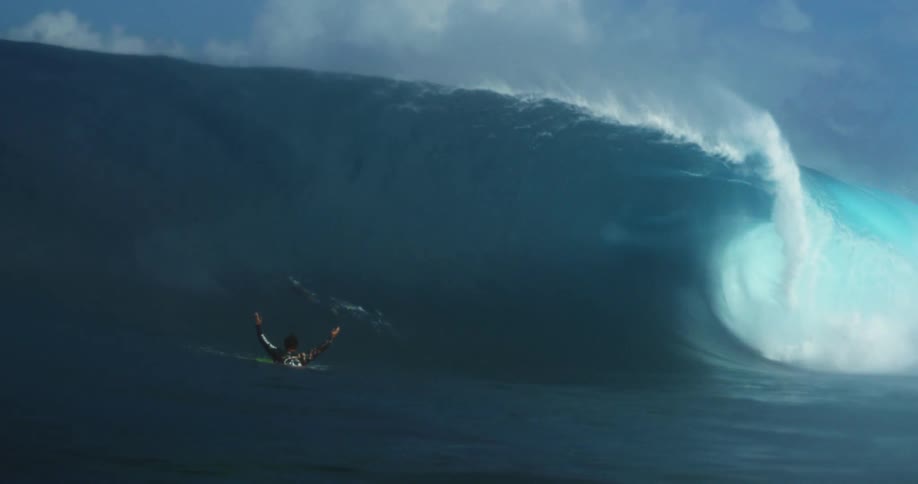 Surfer gets off of his surfboard and stands to face a large wave in the ocean