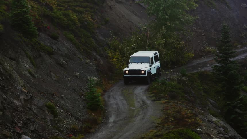 A vehicle driving on a dirt road next to a cliff with trees