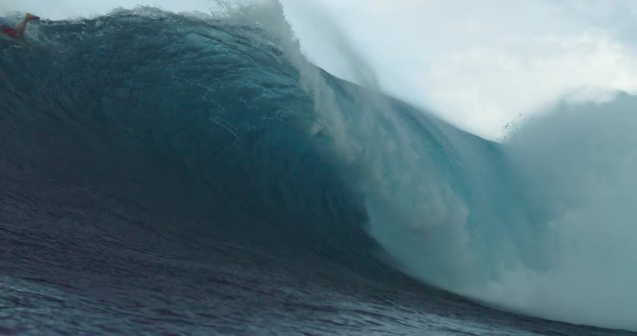 A surfer lies atop their surfboard as it ascends a crashing wave in the ocean during the day