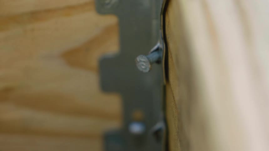 A nail sticking out from a metal bracket joining two wooden boards is progressively hammered inward
