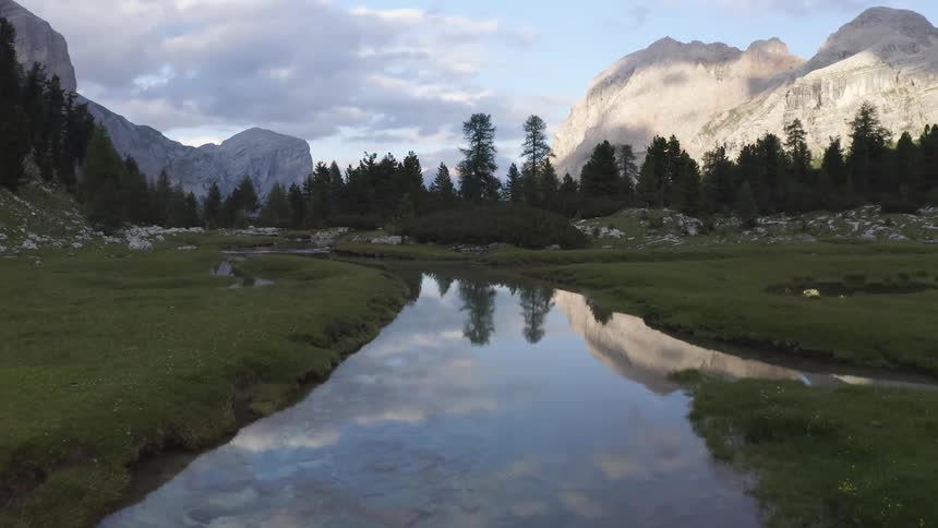 The sky reflects in a narrow creek that runs through a field below a mountain range