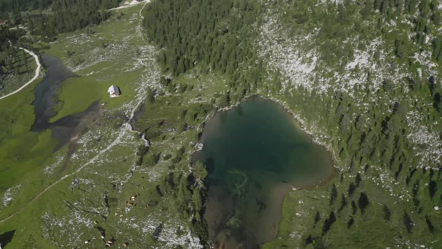 A house sits in a partially snowy field near a lake