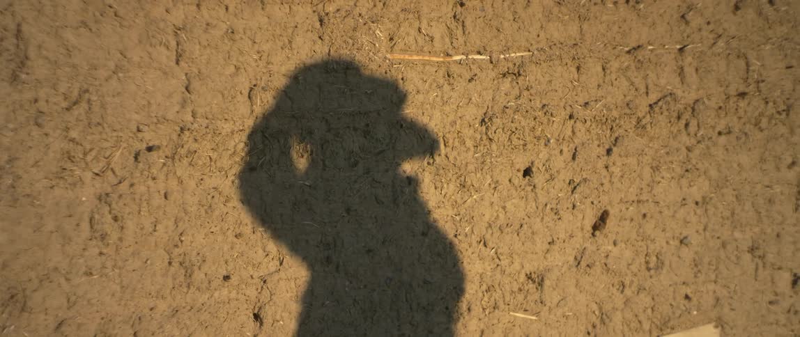 A shadow of a man putting on a hat