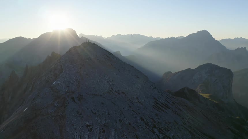 A mountain range with the sun the sky and clouds in the background