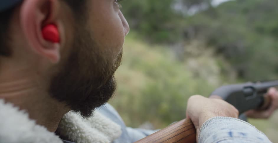 Side view of man with beard and cap shooting shotgun