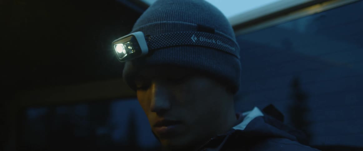 Man wearing a toque and a headlamp turns his head while standing next to a vehicle