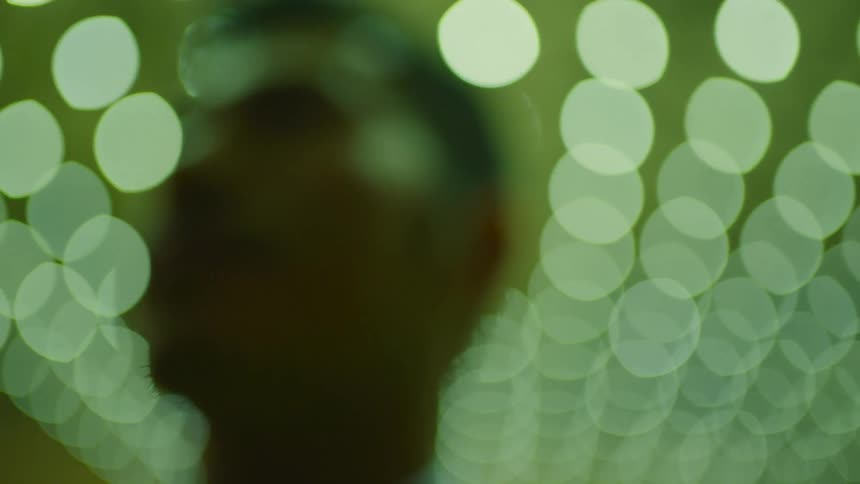 Man with blurred face in front of green bubble lights