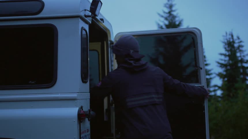 Man wearing a toque and coat retrieves a backpack from the back of a land vehicle