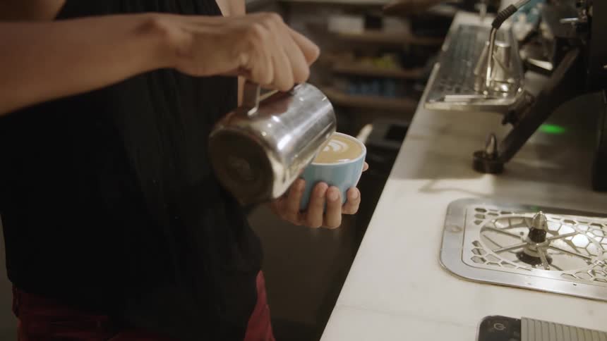 Woman with black shirt pours latte into blue coffee up