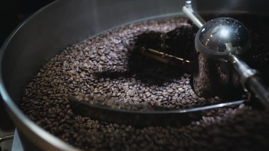 A machine in a room turning coffee beans with a wall and person in the background