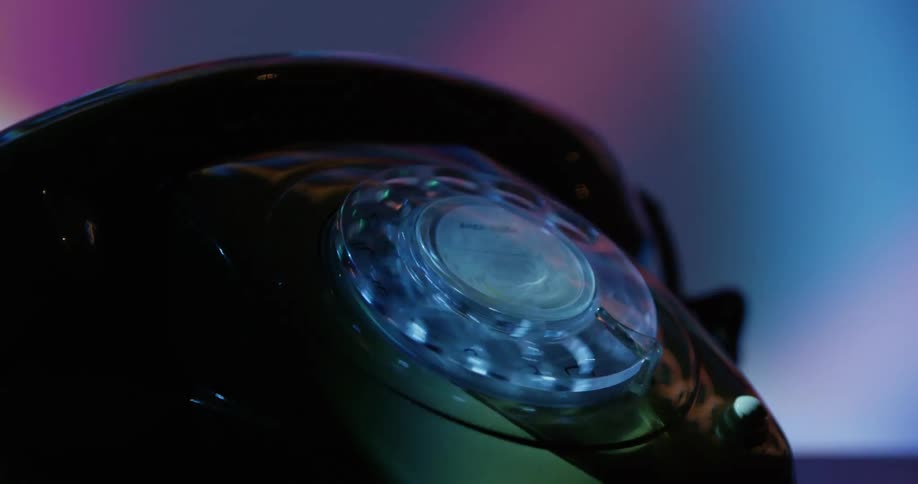 A person uses finger on a vintage rotary phone under moving colorful lights
