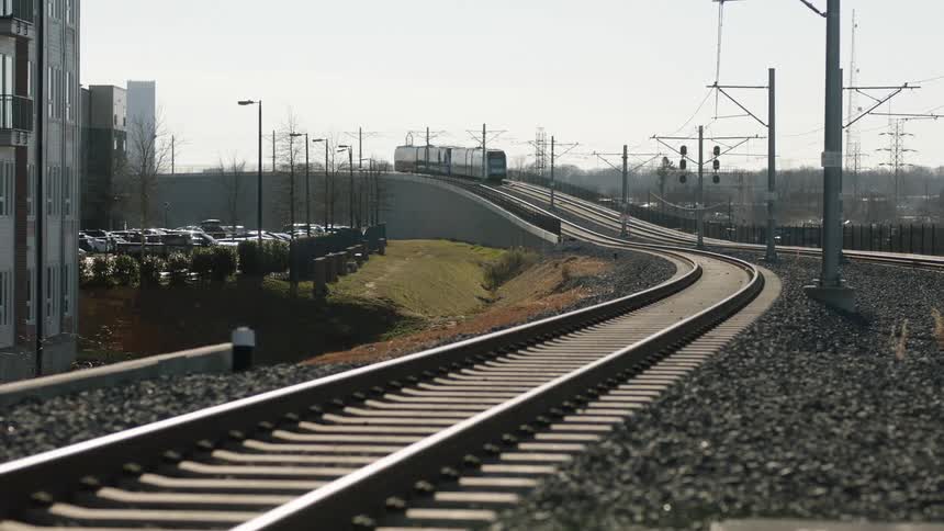 A train travels up an incline past office buildings and parking lots