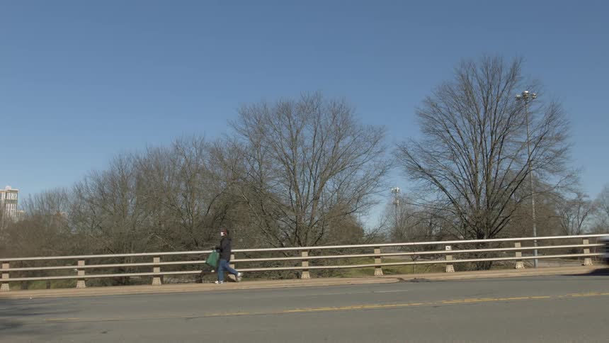 Boy with jeans black coat and green bag crosses the bridge