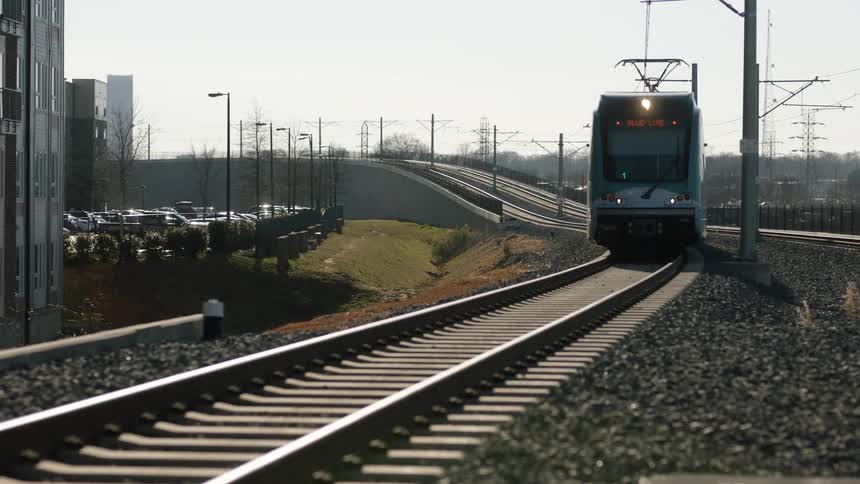 A train passes a building with a parking lot full of vehicles