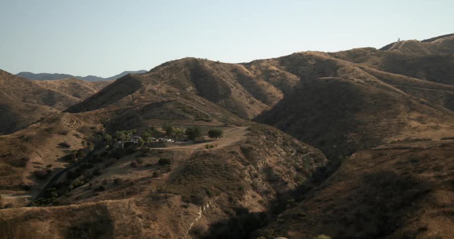 A house in the mountains and a mountain range in the distance under a clear sky