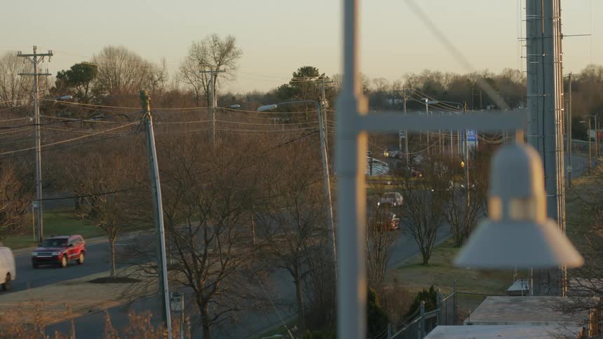 Vehicles drive along road passing leafless trees and businesses