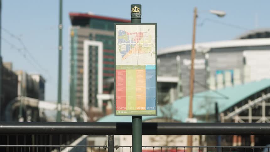 A map on a pole in a city with buildings the sky and clouds in the background
